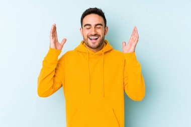 Mavi arka planda izole olmuş genç beyaz adam yüksek sesle gülüyor ve elini göğsüne koyuyor..