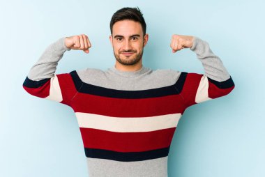 Mavi arka planda izole edilmiş genç beyaz adam güçlü bir hareket sergiliyor kollarıyla, kadınsı gücün sembolü.