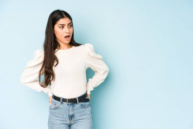 Mavi arka planda izole edilmiş genç bir Hintli kadın gördüğü bir şey yüzünden şok oluyor..