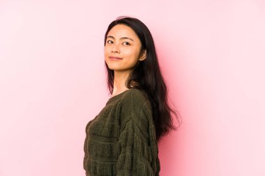 Pembe arka planda izole edilmiş genç Çinli kadın gülümseyen, neşeli ve keyifli bir kenara bakıyor..