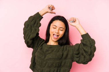 Pembe arka planda izole edilmiş genç Çinli bir kadın özel bir günü kutluyor, atlıyor ve enerjiyle kollarını kaldırıyor..