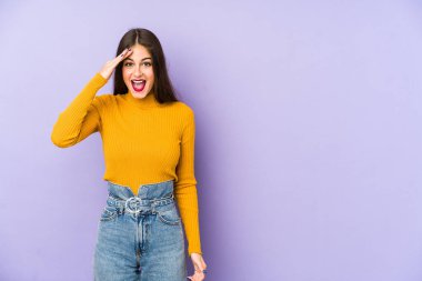 Mor arka planda izole edilmiş genç beyaz kadın yüksek sesle bağırıyor, gözleri açık ve elleri gergin tutuyor..