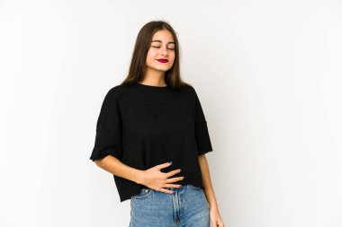 Beyaz arka planda izole genç beyaz kadın karnına dokunuyor, nazikçe gülümsüyor, yemek yiyor ve tatmin oluyor..