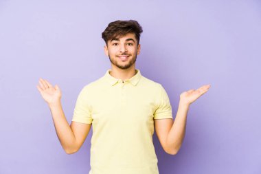 Mor arka planda izole edilmiş genç bir Arap adam kollarıyla ölçek oluşturuyor, mutlu ve kendinden emin hissediyor..