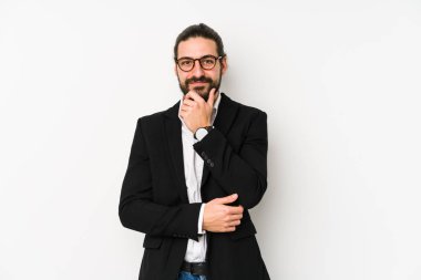 Beyaz bir arka planda izole edilmiş beyaz bir iş adamı mutlu ve kendinden emin gülümsüyor, elleriyle çenesine dokunuyor..