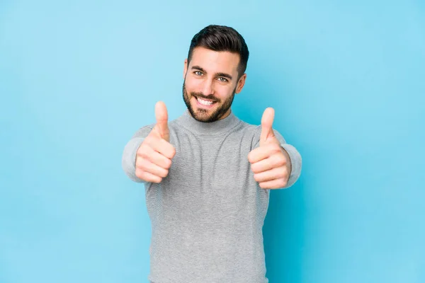 Young caucasian man against a blue background isolated with thumbs ups, cheers about something, support and respect concept.