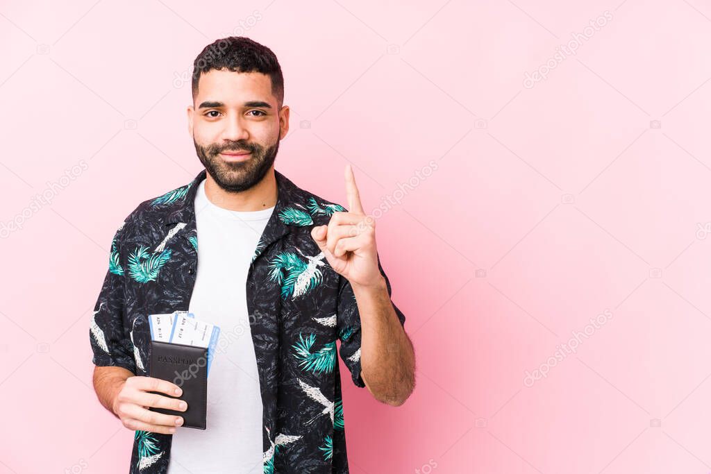 Young arabian cool man holding a boarding passes isolated showing number one with finger.