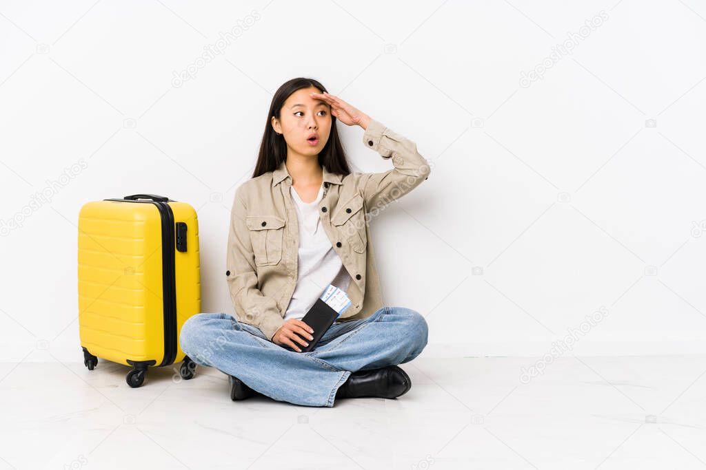 Young chinese traveler woman sitting holding a boarding passes looking far away keeping hand on forehead.
