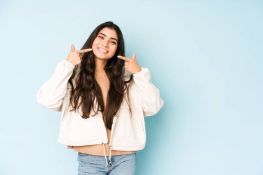 Mavi arka plandaki genç Hintli kadın gülümsüyor, parmaklarını ağıza doğrultuyor..