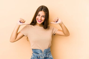 Beyaz tenli genç bir kadın bej arka planda izole edilmiş gururlu ve kendinden emin hissediyor, örnek olarak..