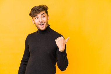 Genç Arap adam sarı arka plan noktalarında izole edilmiş, başparmak uzakta, gülüyor ve kaygısız..