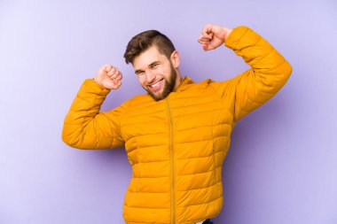 Mor arka planda izole genç adam özel bir günü kutluyor, atlıyor ve enerji ile kollarını kaldırıyor..