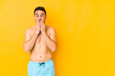 Sarı arka planda mayosu olan genç beyaz bir adam. Kafkasyalı genç, ağzı ellerle kaplanmış, yeni bir şey keşfetmeye hevesli..