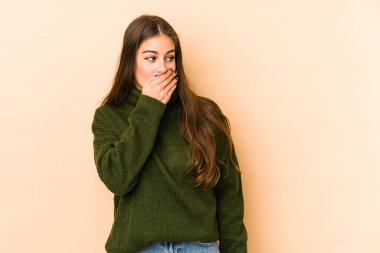 Beyazlı genç bir kadın bej arka planda izole edilmiş. Düşünceli bir şekilde bir fotokopi odasına bakıyor. Ağzını eliyle kapatıyor..