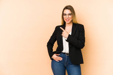 Orta yaşlı iş kadını bej arka planda izole edilmiş gülümseyen ve işaret eden boş alanda bir şey gösteriyor..