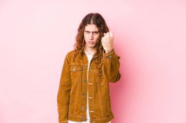 Genç, uzun saçlı, yalnız poz veren, kameraya yumruğunu gösteren, agresif yüz ifadesi olan bir adam..