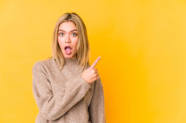 Sarı arka planda izole edilmiş genç sarışın kadın yan tarafı işaret ediyor.