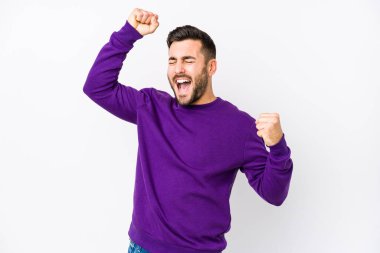 Beyaz arka planda genç beyaz bir adam özel bir günü kutluyor, atlıyor ve enerjiyle kollarını kaldırıyor..