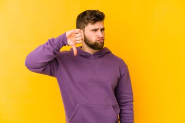 Sarı arka planda izole edilmiş genç beyaz adam baş parmağını aşağı gösteriyor, hayal kırıklığı konsepti..