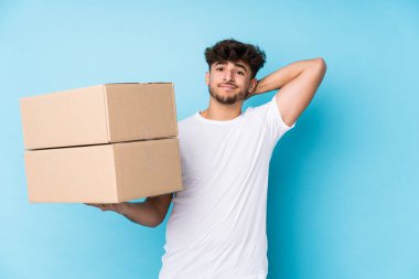 Genç Arap adam kutuları tutuyor. Kafasının arkasına dokunuyor, düşünüyor ve bir seçim yapıyor..