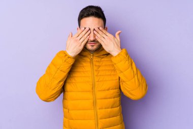 Mor arka planda izole edilmiş genç beyaz adam elleriyle gözlerini kapatmaktan korkuyor..