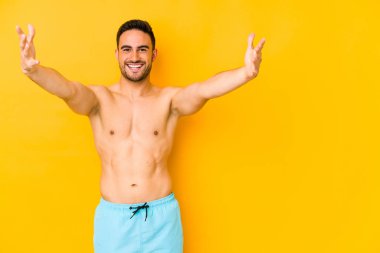 Sarı arka planda mayosu olan genç beyaz bir adam zafer ya da başarı peşinde koşan Kafkasyalı genç bir adam şaşırdı ve şok oldu..