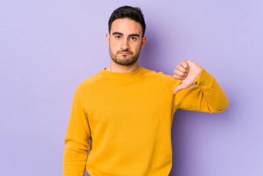 Mor arka planda izole genç beyaz adam baş parmağını aşağı gösteriyor, hayal kırıklığı konsepti.