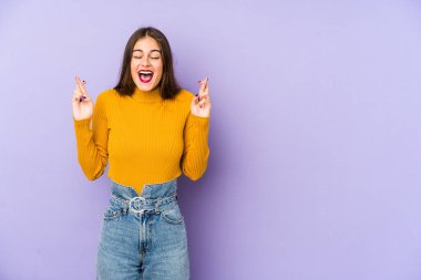 Mor arka planda izole edilmiş beyaz bir kadın şans dilemek için parmaklarını çapraz yapıyor.