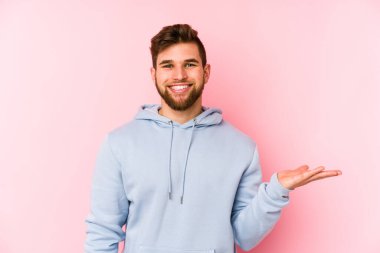 Pembe arka planda izole edilmiş genç beyaz bir adam bir palmiye üzerinde fotokopi alanı ve belinde başka bir el tutuyor..