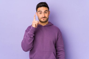Mor arka planda izole genç beyaz adam parmak ile bir numara gösteriyor.