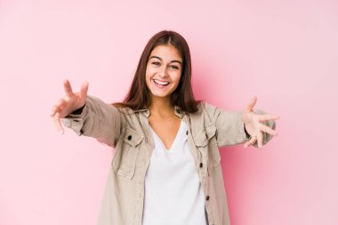 Pembe arka planda poz veren beyaz bir kadın kameraya sarılıyor..