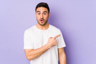 Mor arka planda izole edilmiş genç beyaz adam yan tarafı işaret ediyor.