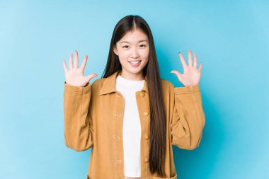 Mavi arka planda poz veren Çinli genç bir kadın 10 numarayı elleriyle gösteriyor..