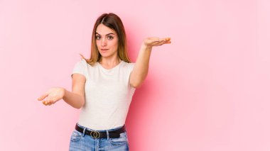 Pembe arka planda izole edilmiş genç beyaz kadın kollarıyla ölçek oluşturuyor, mutlu ve kendinden emin hissediyor..