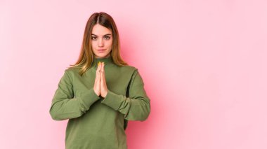 Pembe arka planda izole edilmiş genç beyaz kadın dua ediyor, bağlılık gösteriyor, dindar biri ilahi ilham arıyor..