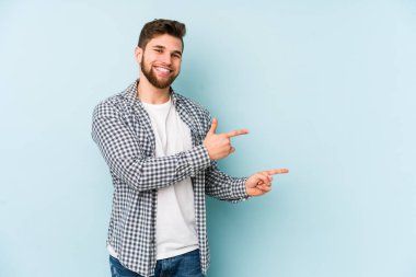 Kafkasyalı genç adam mavi arka planda izole edilmiş. İşaret parmağıyla işaret ettiği için heyecanlı..