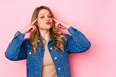 Pembe arka planda izole edilmiş genç beyaz kadın bir göreve odaklanmış, parmaklarını işaret ediyor..