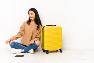 Genç Çinli gezgin bir bavulla yerde oturuyor. Tuhaf ve dostane bir dille..