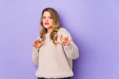 Young caucasian woman isolated on purple background being shocked due to an imminent danger clipart