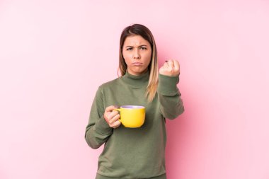 Kameraya yumruğunu gösteren bir kahve tutan beyaz bir kadın, agresif bir yüz ifadesi..