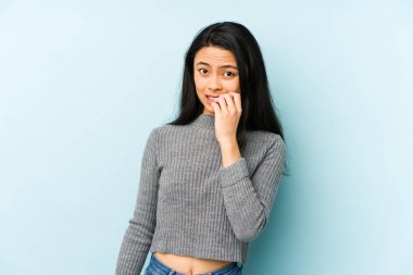 Mavi arka planda izole edilmiş, tırnak yiyen, gergin ve endişeli genç Çinli bir kadın..