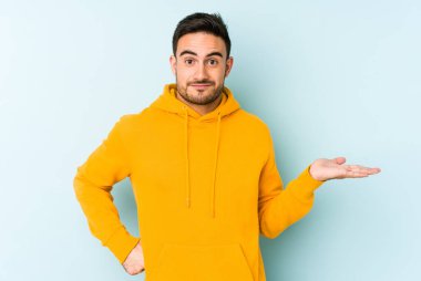 Mavi arka planda izole edilmiş genç beyaz bir adam bir palmiye üzerinde fotokopi alanı ve belinde bir el daha gösteriyor..