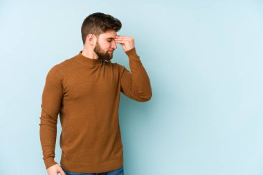 Kafkasyalı genç bir adam mavi arka planda izole edilmiş, başı ağrıyor, yüzüne dokunuyor..