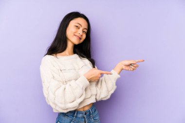 Mor bir arka planda izole edilmiş genç Çinli kadın işaret parmaklarıyla işaret ederek heyecanlanıyor..