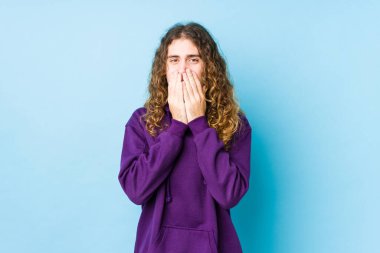 Uzun saçlı adam yalnız poz veriyor. Bir şeye gülüyor, elleriyle ağzını kapatıyor..