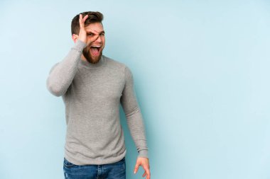 Kafkasyalı genç adam mavi arka planda izole edildi. Heyecanlı görünüyor..