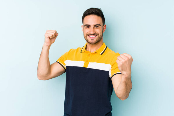 Young caucasian man isolated on blue background cheering carefree and excited. Victory concept.