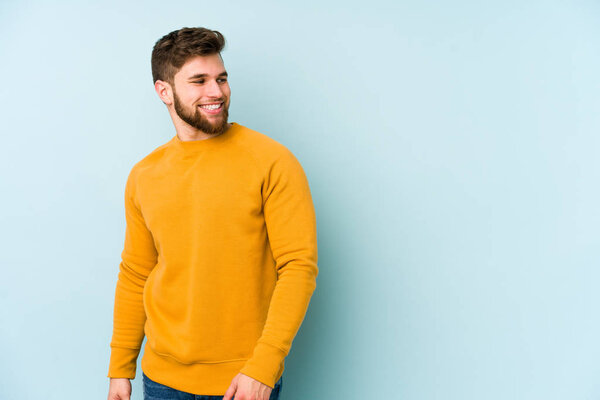 Young caucasian man isolated on blue background looks aside smiling, cheerful and pleasant.