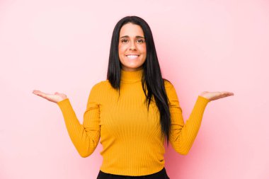 Pembe arka planda izole edilmiş genç beyaz kadın kollarıyla ölçek oluşturuyor, mutlu ve kendinden emin hissediyor..