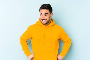 Mavi arka planda izole edilmiş genç beyaz adam gülüyor ve gözlerini kapıyor, rahatlamış ve mutlu hissediyor..